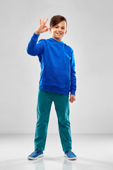 Wall Mural - childhood, gesture and people concept - portrait of smiling boy in blue hoodie showing ok hand sign over grey background