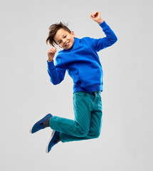 childhood, expressions and people concept - portrait of smiling boy in blue hoodie jumping over grey background