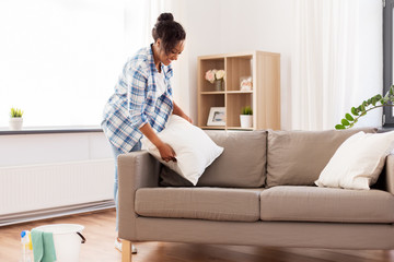 Sticker - household, housework and cleaning concept - african american woman arranging sofa cushions at home