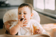 © komokvm - The baby in the kitchen greedily eats delicious cream cones filled with vanilla cream licks her fingers