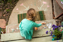 A Preschool Aged Girl Drawing With Chalk Outdoors On The Cement.