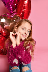 Close-up of cute girl in a studio, smiling widely and playing with pink balloons. She wears sweater and jeans. She is having fun party