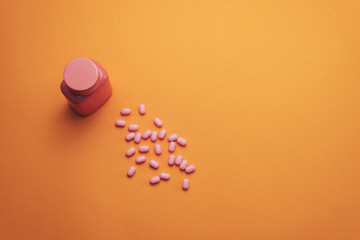 Poster - Beautiful pink bottle and pink pills on a orange background. Top view.