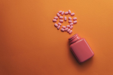 Poster - Beautiful pink bottle and pink pills on a orange background. Top view.