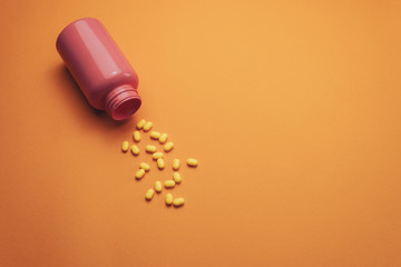 Poster - Beautiful pink bottle and yellow pills on a orange background. Top view.
