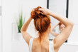 Young redhead woman tying her hair up in a bun