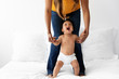 © Lisa Tichané - Laughing baby standing up on bed while holding his mother's hands
