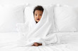 © Lisa Tichané - Black baby sitting on bed wrapped in towel after bath