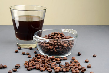 A glass of black coffee with roasted coffee beans