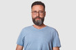 © sementsova321 - Close up portrait of dark haired serious young male with beard, man looks confidently at camera, dressed casual gray t shirt and round glasses, isolated over white background. People concept.