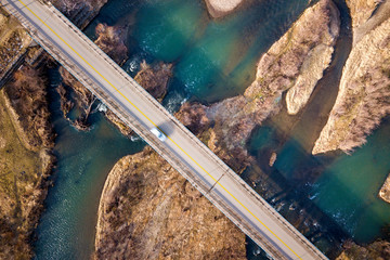 Wall Mural - Aerial view of white bridge with moving car over blue water and stony islands.