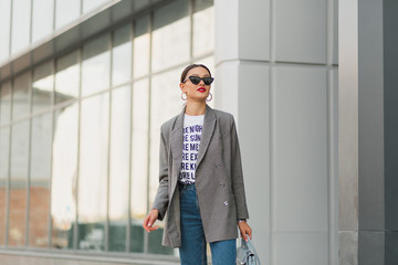 Stylish businesswoman wearing white t-shirt, jacket and jeans got out from business center and going for lunch 