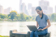 © TeTe Song - Portrait of pretty young woman sitting on bench  in park during summer day while using laptop of online shopping.