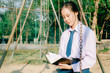 © TeTe Song - Lovely teenage girl wearing school uniform reading book while sitting on a swing at the park .