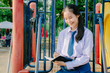 © TeTe Song - Lovely teenage girl wearing school uniform writing book while sitting on a swing at the park.