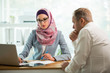 © Suzi Media  - Coworkers meeting in office. Stylish woman in hijab making conversation at desk with man in white modern office. Muslim businesswoman in eyeglasses interviewing man.