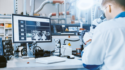 Electronics Factory Worker in White Work Coat Inspects a Printed Circuit Board on a Computer Screen that is connected to a Digital Microscope. High Tech Factory Facility.