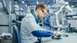 © Gorodenkoff - Young Man in Blue and White Work Coat is Using Plier to Assemble Printed Circuit Board for Smartphone. Electronics Factory Workers in a High Tech Factory Facility.