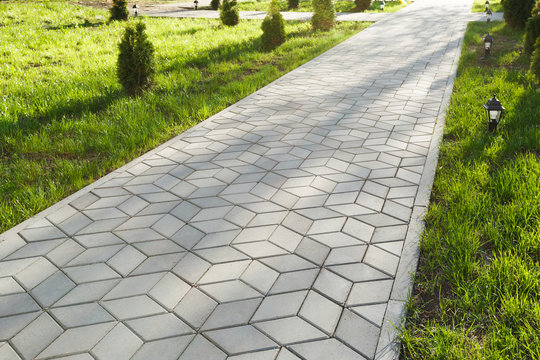 the footpath in the park is paved with diamond shaped concrete tiles. on the lawn - small decorative