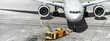 airplane on airport runway with pushback tractor attached to plane nose gear aerial top front view passenger jet engine aircraft towing by ground vehicle to terminal gate black and white wide banner