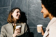 © Westend61 - Two happy women with takeaway coffee talking at a wall