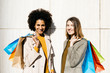© Westend61 - Portrait of two happy women with shopping bags standing at a wall