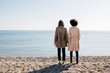 © Westend61 - Back view of two friends standing on the beach looking at the sea