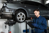 Fototapeta Mapy - Technician checking car on hydraulic lift at automobile repair shop