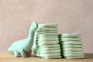 Wall Mural - stacks of diapers and toy dinosaur on table against color background. baby accessories