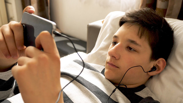 teen boy with smart phone listening or talking on sofa indoor. teenager and social media concept