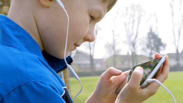 sad teen boy with smart phone listening or talking while sitting in british park. teenager and social media concept