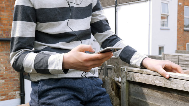 teen boy with smart phone listening or talking while sitting in british backyard garden. teenager and social media concept