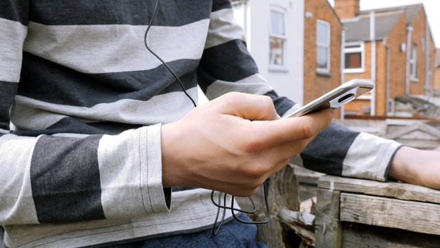 teen boy with smart phone listening or talking while sitting in british backyard garden. teenager and social media concept