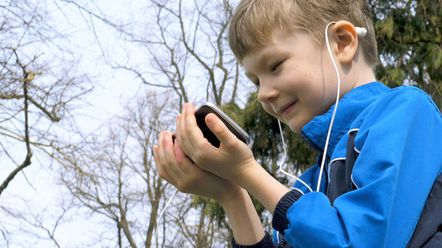 smiling teen boy with smart phone listening or talking in british park. teenager and social media concept