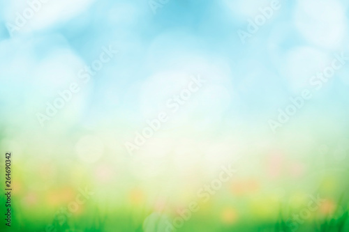 Abstract background with green grass and flowers over sunny blue sky