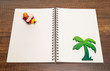 Red and yellow wooden airplane on blank white notebook with green palm tree