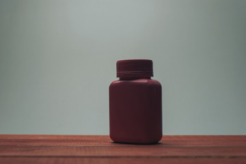 Poster - Pink bottle for pills on a red wooden table and gray background.