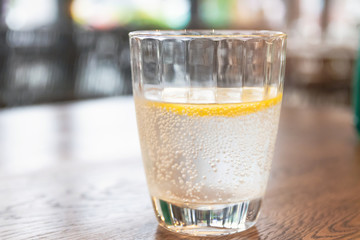 Glass of sparkling water with lemon slices on wooden brown table with blur bokeh background.