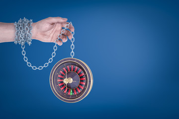 Poster - Male hand chained to a roulette on blue background
