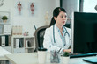© PR Image Factory - asian female doctor working with personal computer and writing on paperwork. Hospital background. chinese woman medical staff wear white robe in clinic office typing online patient document internet.