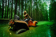 Beautiful blonde girl on a orang ATV rides on the river, standing on the mountain. Around the forest, sand and blue sky.She rides on a green swamp, in the mud and all wet. She's wearing a blue bikini.
