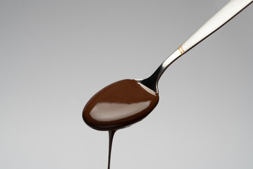 Wall Mural - Liquid chocolate on a spoon on light grey backgiund