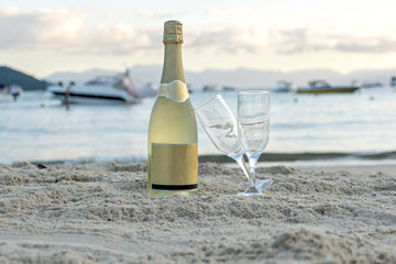 close up of a bottle of sparkling wine with two crossed bowls on the sand of the beach