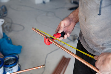 Wall Mural - Closeup worker plumber master measures copper pipes with roulette tape, cut pipe with cutter. Concept installation, changing pipeline, repair, leakage, breaking sewage