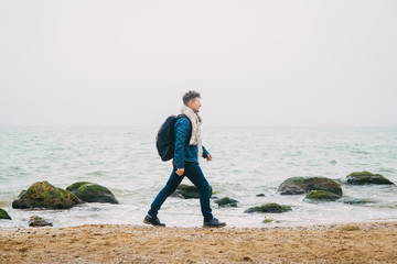 Wall Mural - traveler with a backpack standing near a rock against a beautiful sea with waves, a stylish hipster 