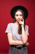 © F8  \ Suport Ukraine - Young thinking woman with black hat standing isolated on red background