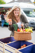 Sympathisch lachende Frau auf dem Markt freudig mit Einkäufen und einem Apfel 