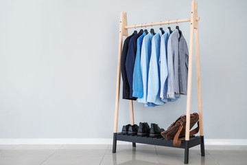 rack with stylish male clothes near light wall