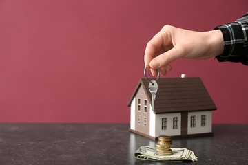 Poster - Female hand with key, figure of house and money on table against color background. Concept of buying real estate