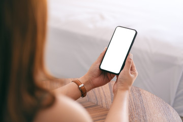 mockup image of a woman holding and using mobile phone with blank screen while sitting beside the be